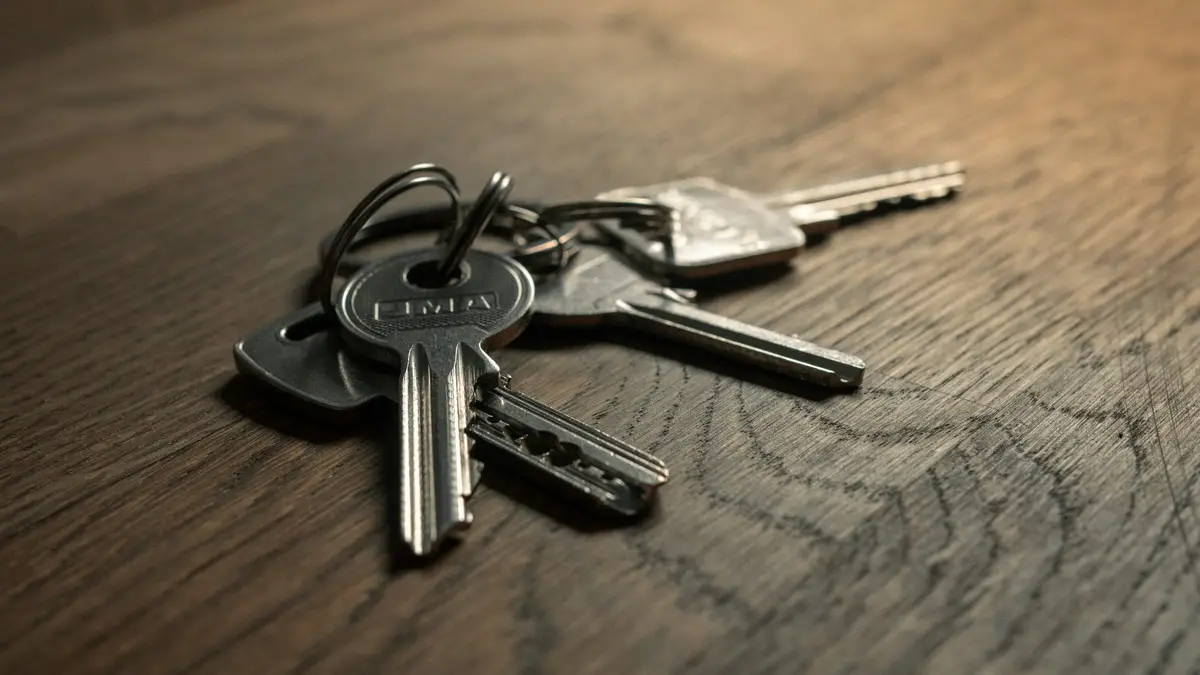 Close-up of a small bunch of silver house keys on a ring resting on a dark wooden surface