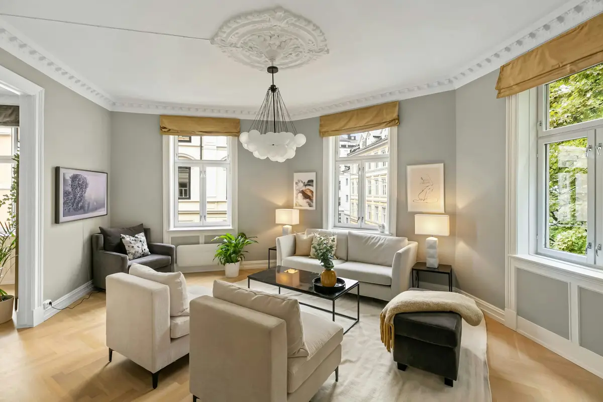 High-ceilinged living room with an ornate plaster cornice and ceiling rose, tall windows with gold roman blinds, cream sofas and a herringbone parquet floor