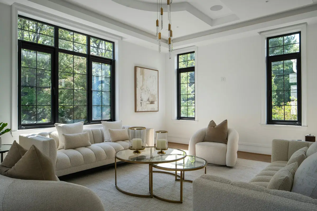 Spacious, light living room with large black-framed windows, cream bouclé sofas, round glass coffee tables and a panelled ceiling with brass pendant lights